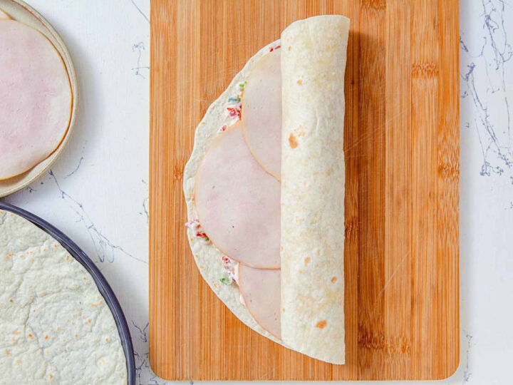 Sliced turkey layered over the cream cheese mixture on a tortilla, partially folded.