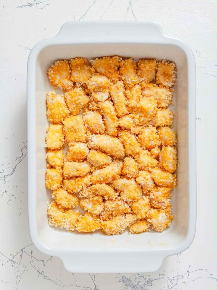 Breaded chicken pieces arranged in a baking dish before cooking.