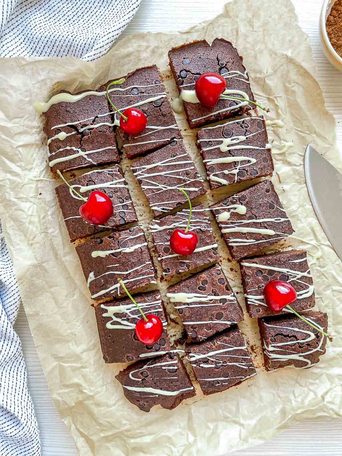 Beer brownies cut into squares, topped with white chocolate drizzle and fresh cherries on parchment paper