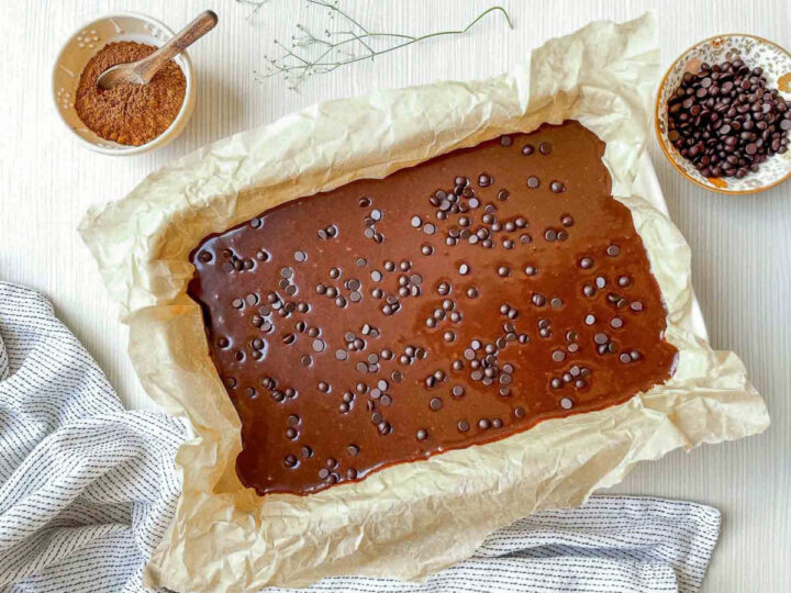 Chocolate brownie batter spread in a parchment-lined pan and topped with chocolate chips