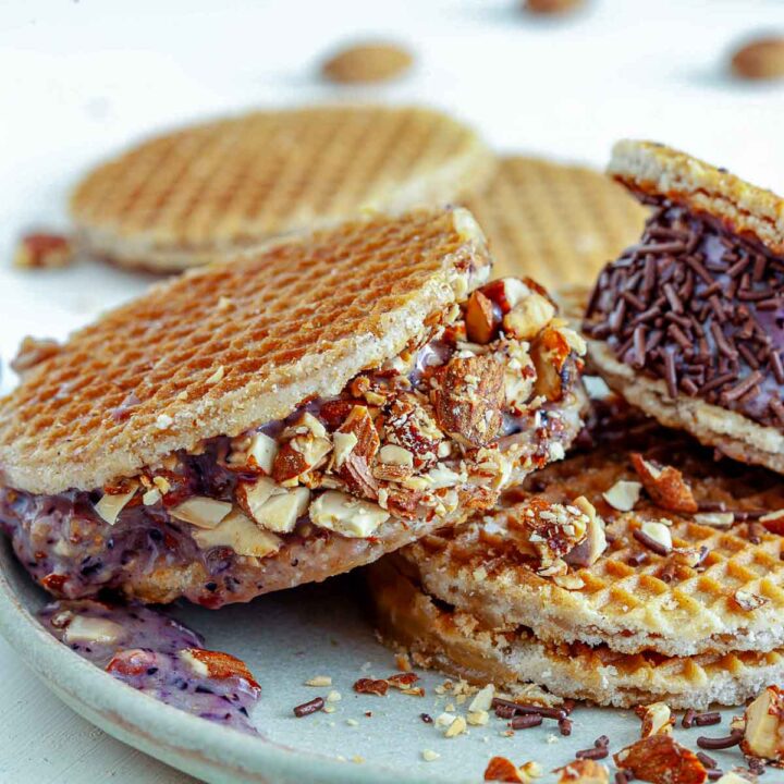 Blueberry almond ice cream waffle sandwich rolled in chopped almonds and chocolate sprinkles, with waffle cookies stacked in the background