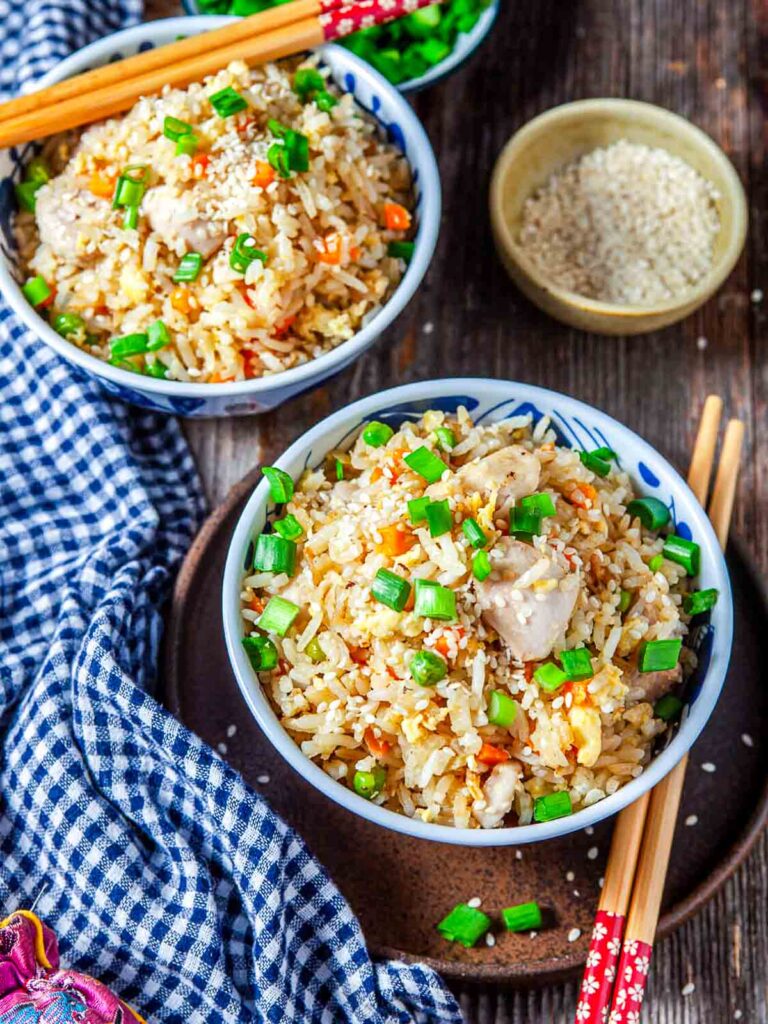 Two bowls of chicken fried rice topped with green onions and sesame seeds.