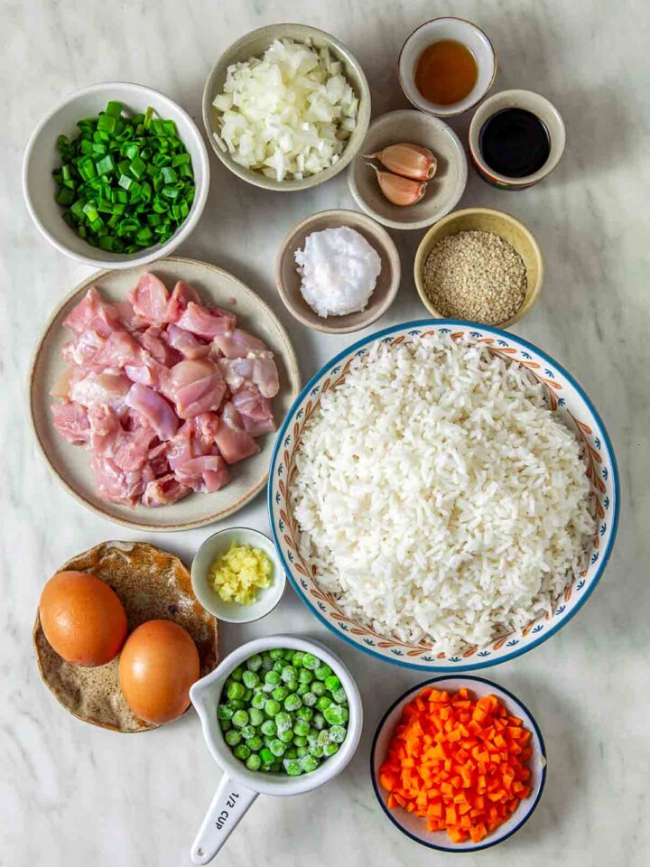 Chicken fried rice ingredients including rice, chicken, eggs, vegetables, and sauces arranged on a countertop.