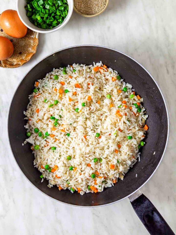 Rice stir-frying in a skillet with peas and diced carrots.