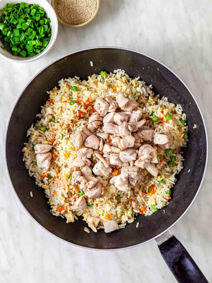 Cooked chicken added to fried rice with vegetables in a skillet.