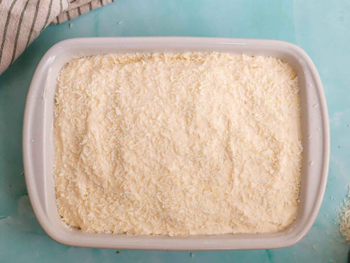 Fully frosted coconut cake topped with shredded coconut in a baking dish.