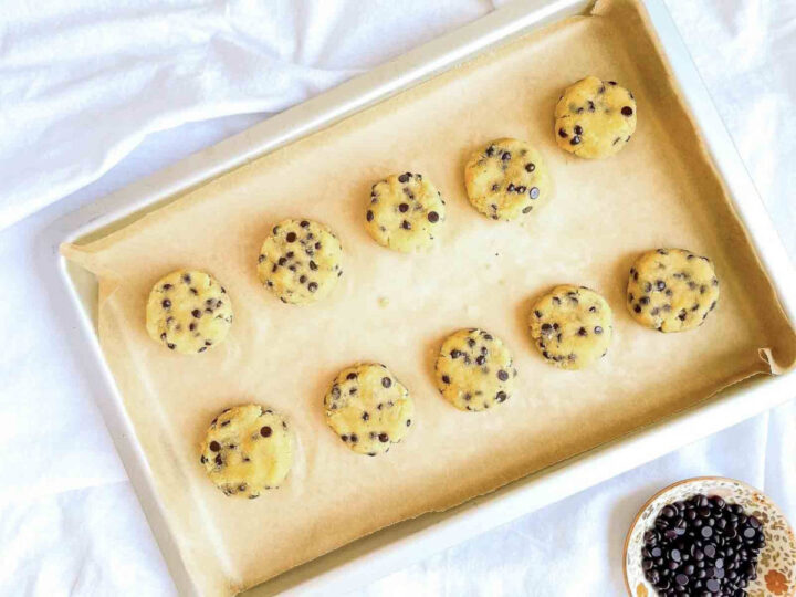 Unbaked coconut flour chocolate chip cookie dough rounds spaced on a parchment-lined baking sheet before baking