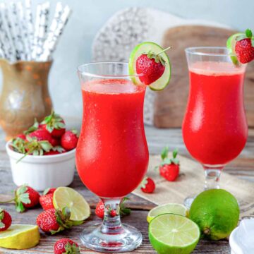 Two frozen strawberry daiquiris, garnished with lime and fresh strawberries.