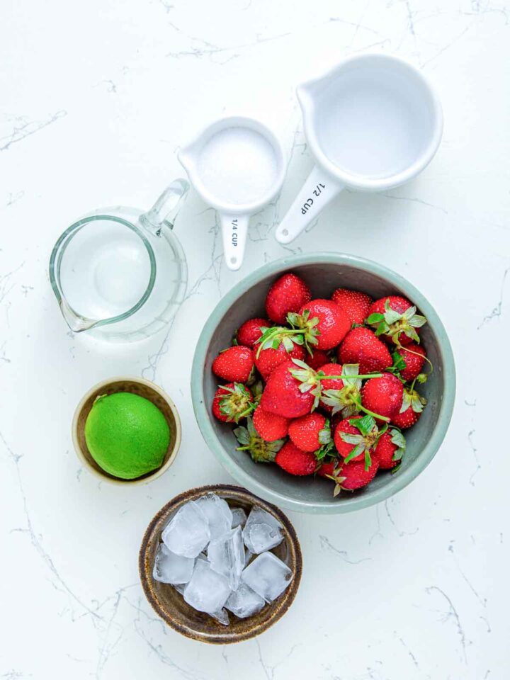Strawberries, lime, ice, sugar, and liquid ingredients for daiquiri.