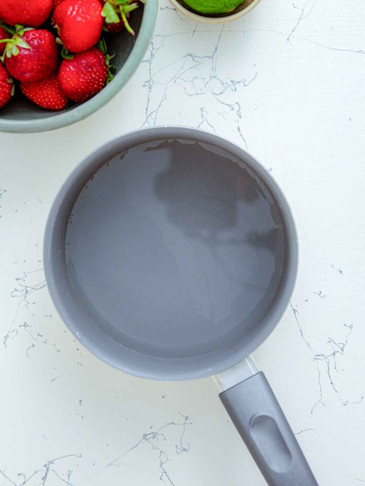 Saucepan with water next to fresh strawberries.