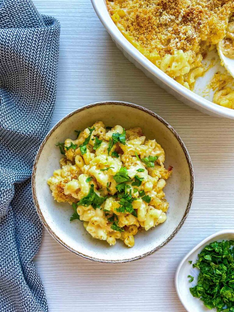 Bowl of baked macaroni and cheese topped with fresh herbs.