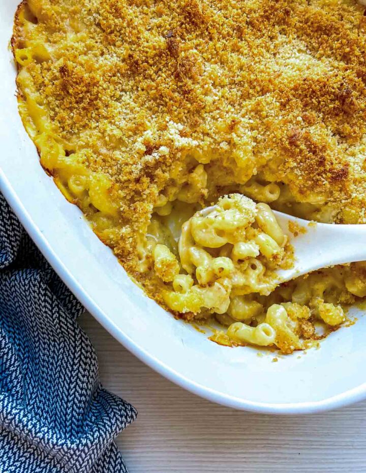 Spoon scooping creamy baked macaroni and cheese with crispy topping.