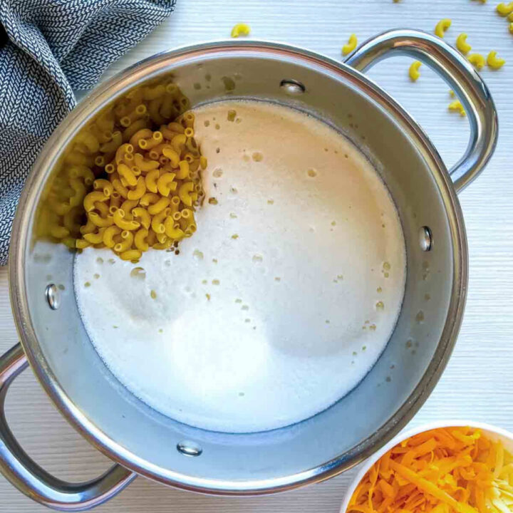 Elbow macaroni added to milk mixture in a pot.