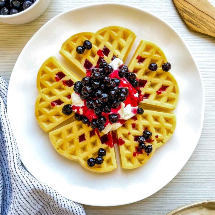 Golden waffle topped with whipped cream, blueberry compote, and fresh blueberries, sliced and ready to serve.