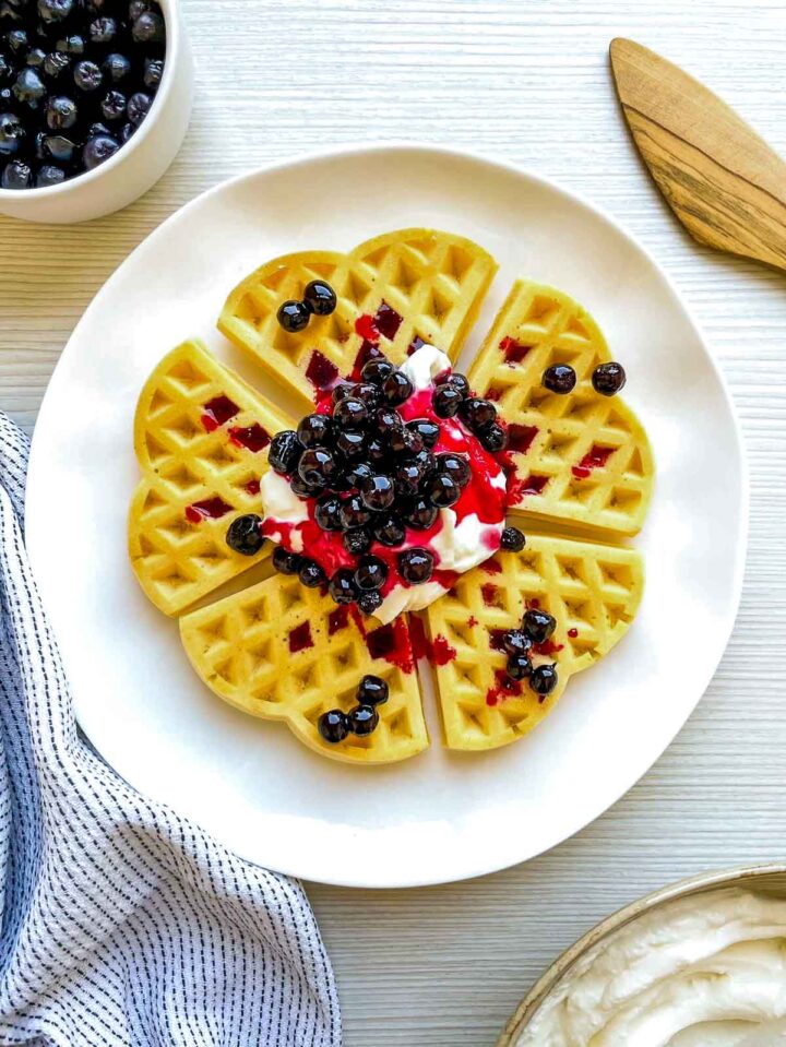 Lemon blueberry cheesecake waffle topped with cream and juicy blueberries, beautifully plated and ready to enjoy.