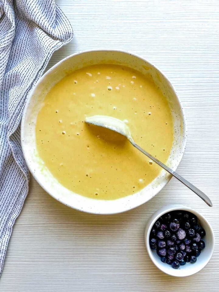 Smooth waffle batter in a bowl with blueberries nearby, ready for cooking.