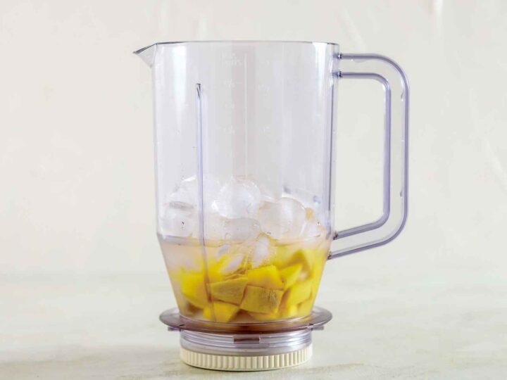 Blender with mango, ice, and liquid ingredients.