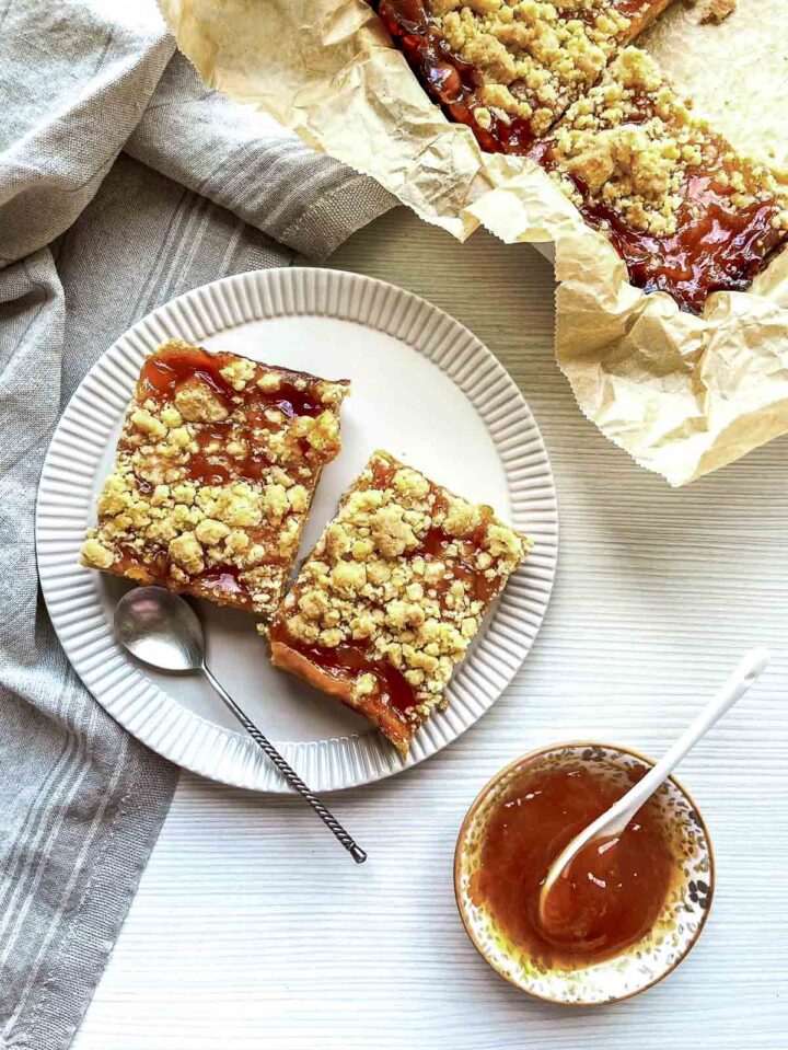 Top view of peach crumble bars with a buttery crumb topping on a plate, served with a bowl of peach jam and spoon.