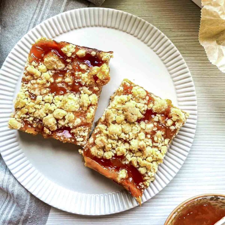 Two peach crumble bars with a buttery crumb topping and glossy peach filling on a white plate.