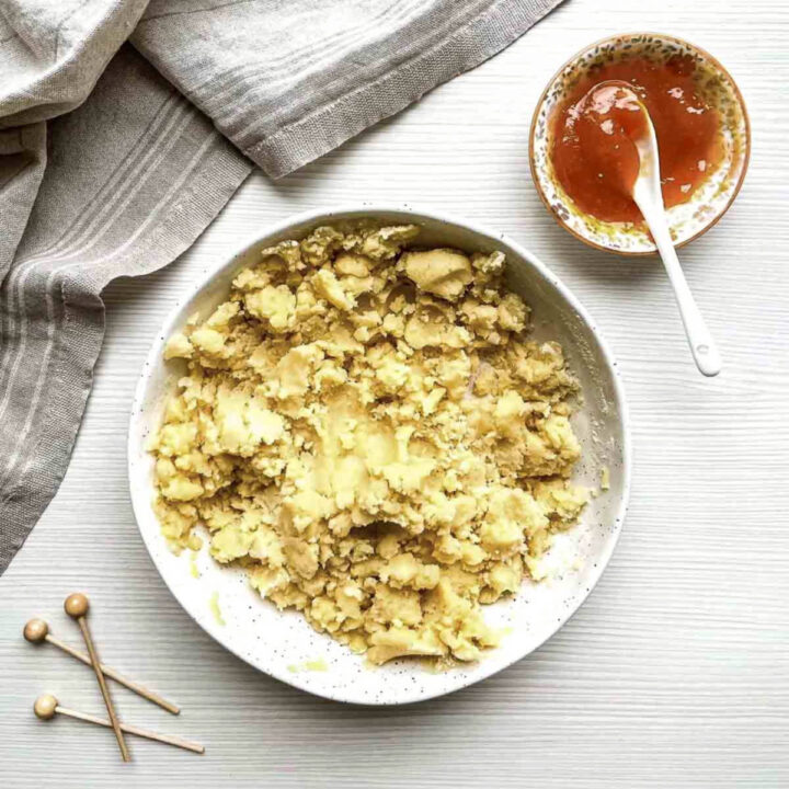 Crumbly dough mixture on a plate beside a bowl of peach jam and spoon.