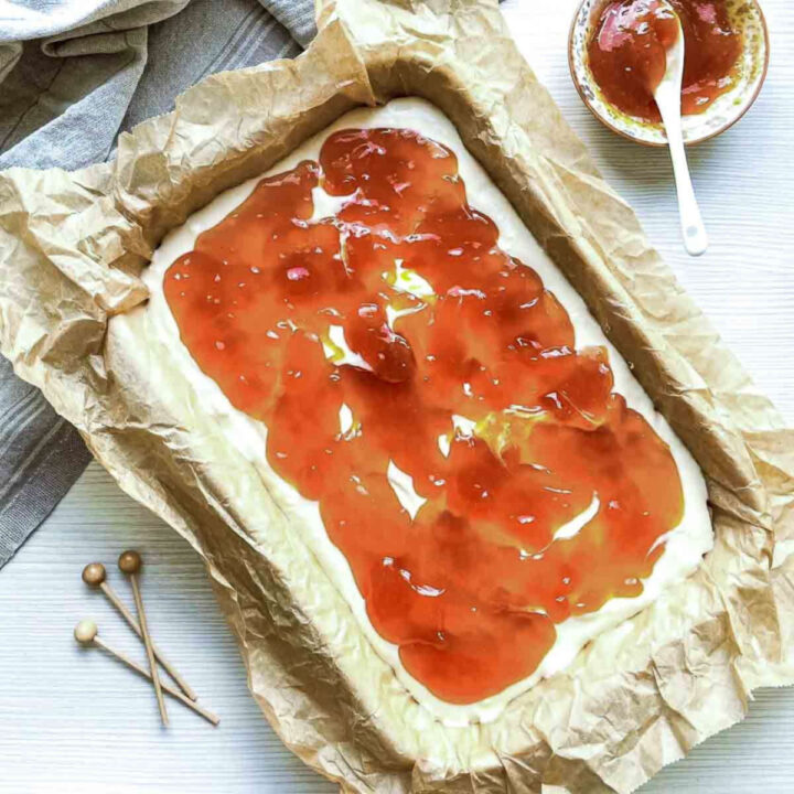 Peach jam spread over cream cheese layer in a parchment-lined baking pan.
