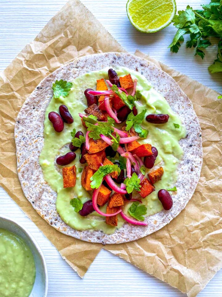 Veggie taco topped with avocado crema, sweet potatoes, red beans, and pickled onions.