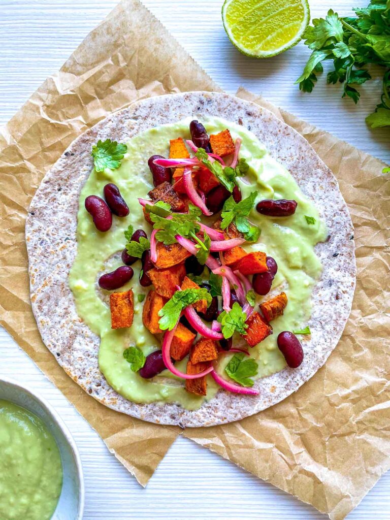 Veggie taco topped with avocado crema, sweet potatoes, red beans, and pickled onions.