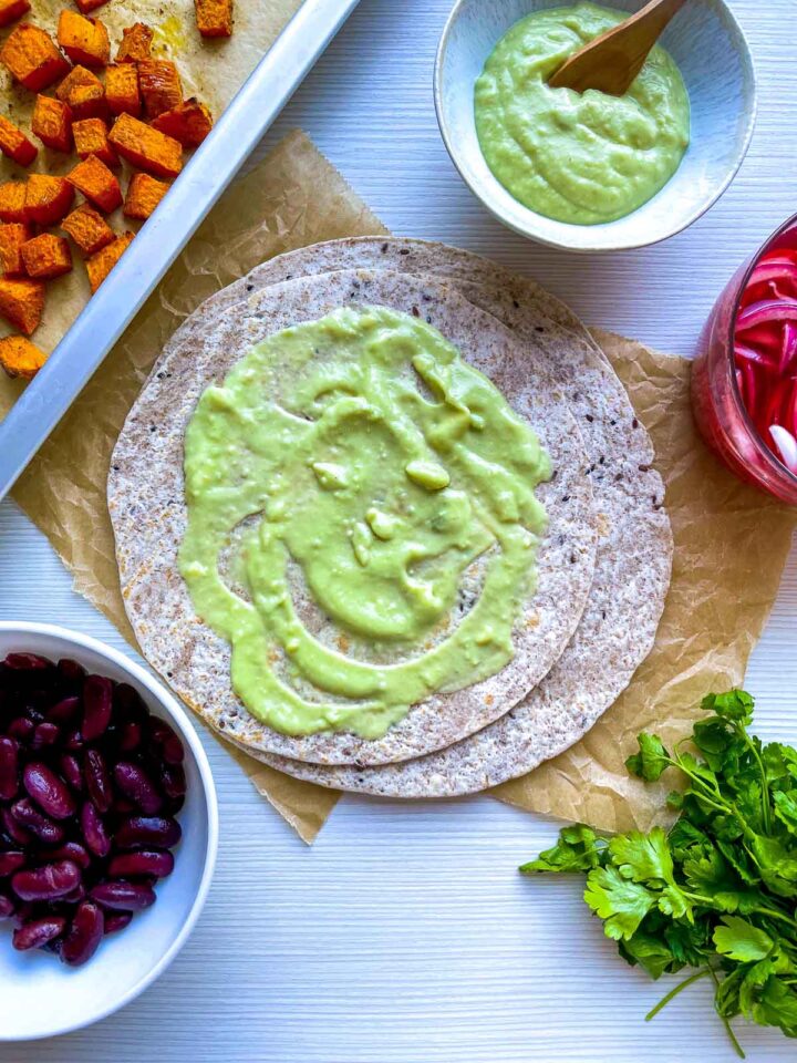 Assembled taco layered with sweet potatoes, red beans, pickled onions, and herbs.
