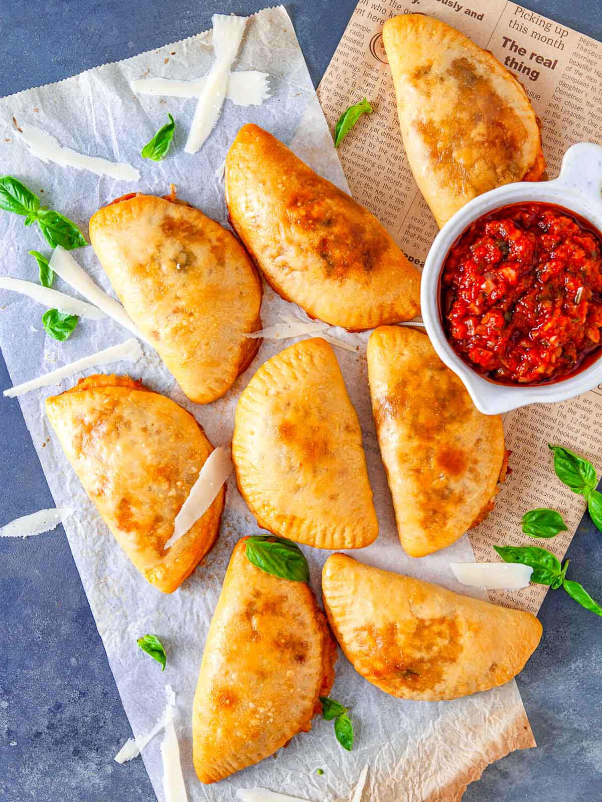 Baked sausage pizza pockets arranged on parchment with marinara sauce and basil leaves.