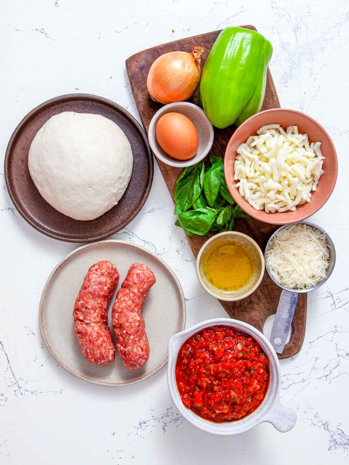 Ingredients for sausage pizza pockets including dough, sausage, mozzarella, onion, green pepper, egg, and marinara sauce.