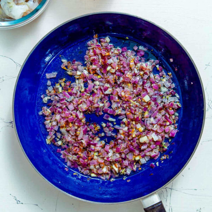 Chopped red onions and garlic sautéing in olive oil in a blue skillet.