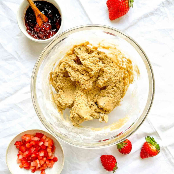 Cookie dough in a glass bowl with chopped strawberries and strawberry jam nearby