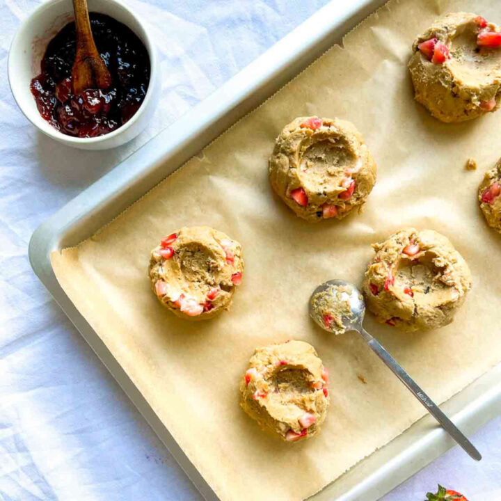 Strawberry cheesecake cookie dough shaped with wells on a parchment-lined baking sheet, ready to be filled