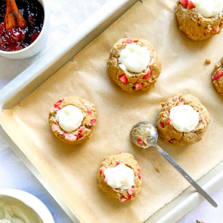 Strawberry cheesecake cookie dough rounds topped with a dollop of cream cheese filling on a parchment-lined baking sheet before baking