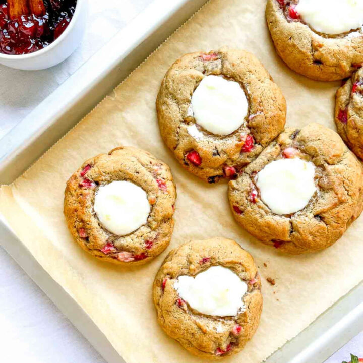 Freshly baked strawberry cheesecake cookies with golden edges and a creamy cheesecake center, cooling on a parchment-lined baking tray
