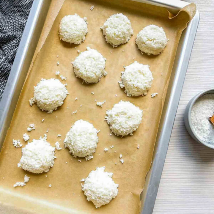 Unbaked coconut macaroon dough rounds arranged on a parchment-lined baking sheet before baking