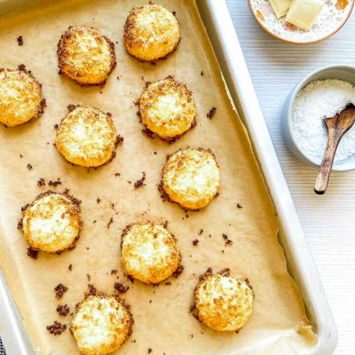 Freshly baked coconut macaroons with golden, toasted edges cooling on a parchment-lined baking sheet
