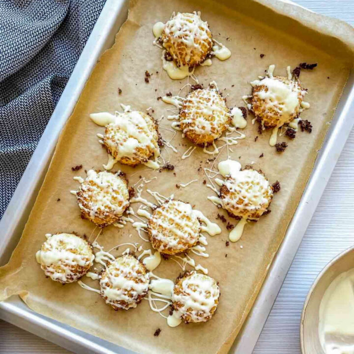 Coconut macaroons drizzled with melted white chocolate on a parchment-lined baking sheet