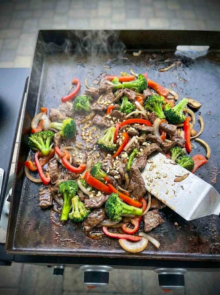 Beef and broccoli stir fry cooking on a Blackstone griddle with garlic sauce.
