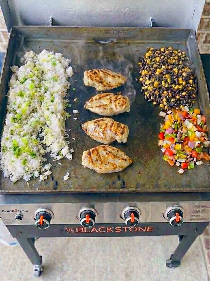 Chicken, rice, beans, corn, and vegetables cooking on a Blackstone griddle.