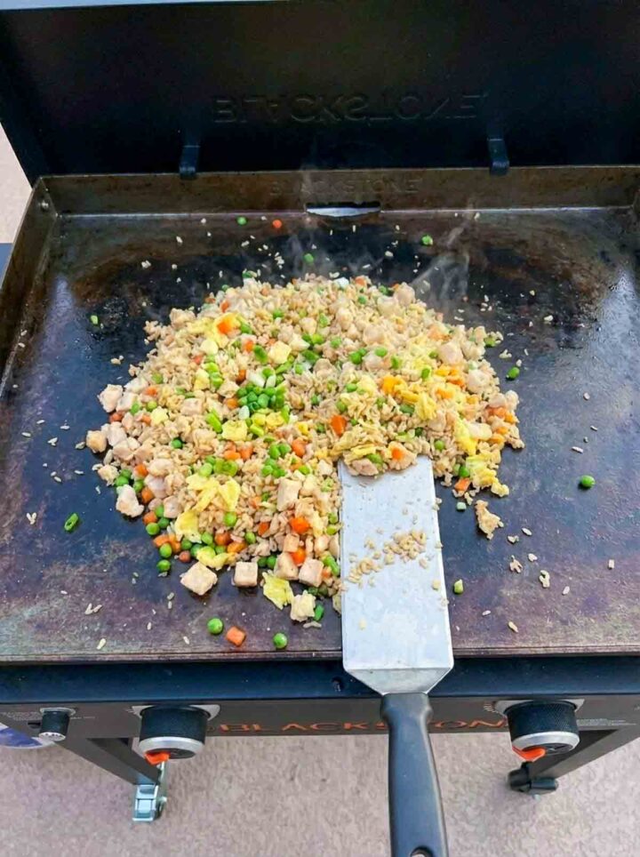 Chicken fried rice with eggs, peas, and carrots cooking on a Blackstone griddle.