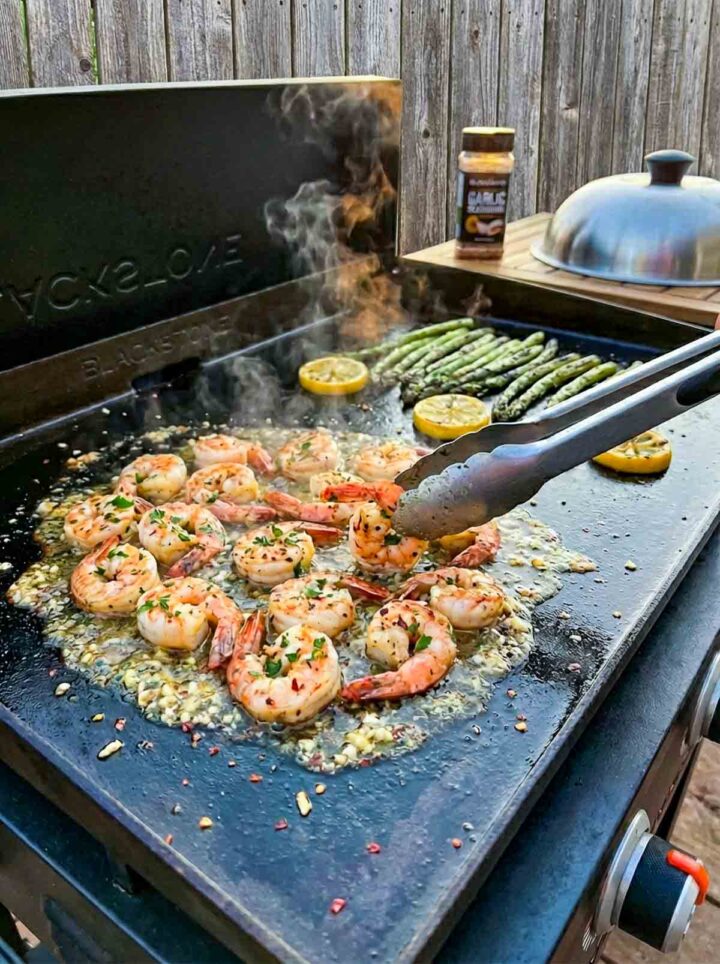 Garlic butter shrimp cooking on a Blackstone griddle with asparagus, lemon slices, and steam rising.