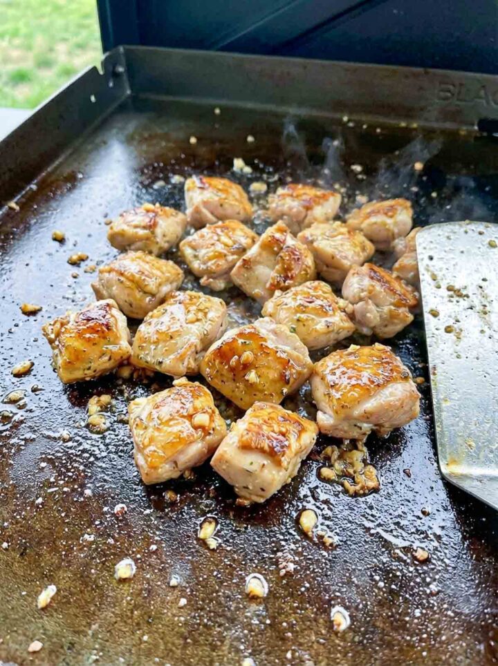 Garlic butter chicken bites sizzling on a Blackstone griddle with golden sear and visible garlic.