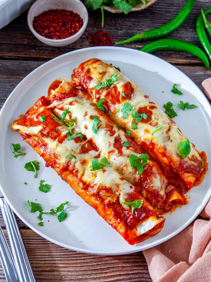 Plate of chicken enchiladas topped with melted cheese, red sauce, and fresh cilantro.