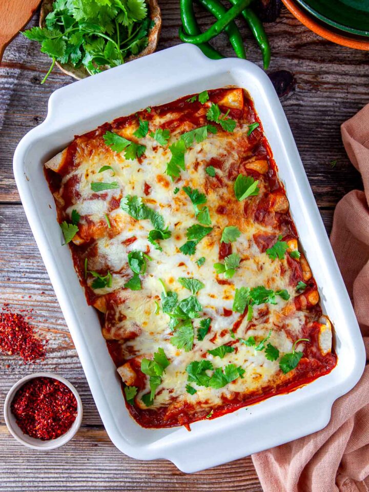 Cheesy chicken enchiladas baked in red sauce and garnished with fresh cilantro in a casserole dish.