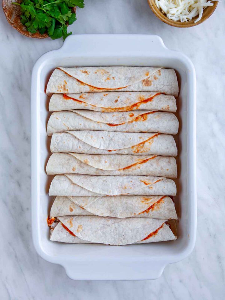 Rolled chicken enchiladas arranged in a baking dish before adding sauce and cheese.