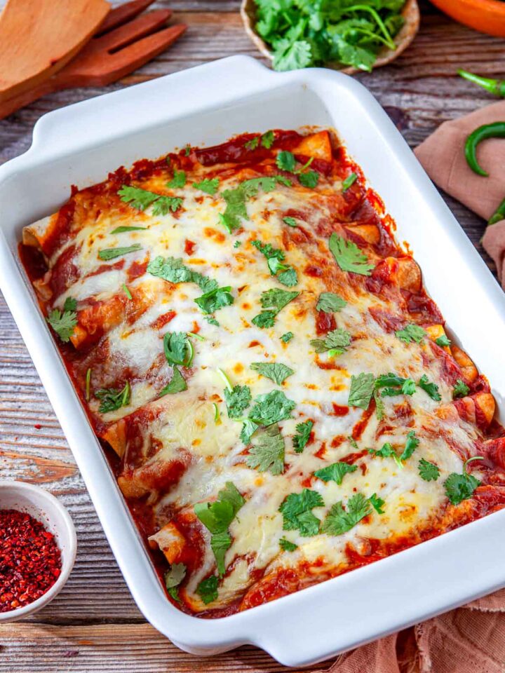 Baked chicken enchiladas in a casserole dish topped with melted cheese and fresh cilantro.