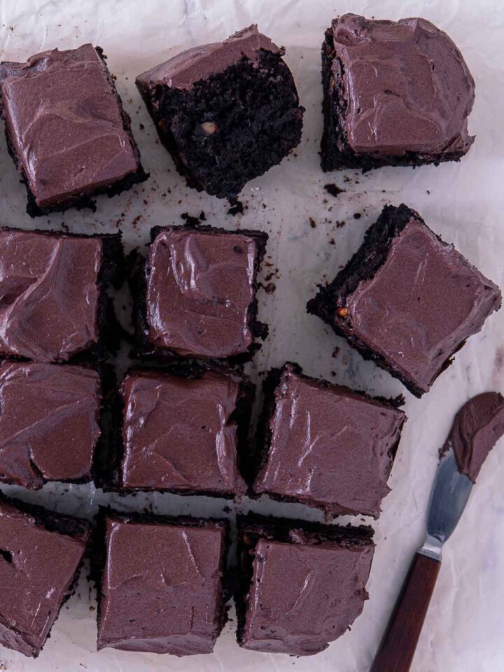 Chocolate walnut brownies cut into squares with chocolate frosting on parchment paper.