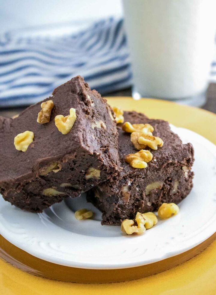 Stacked chocolate walnut brownies on a white plate with walnut pieces on top.