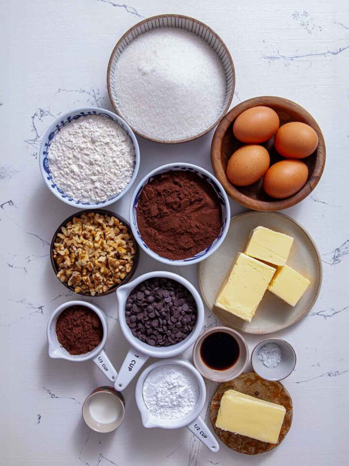 Ingredients for chocolate walnut brownies including cocoa powder, walnuts, chocolate chips, eggs, butter, sugar, and flour.